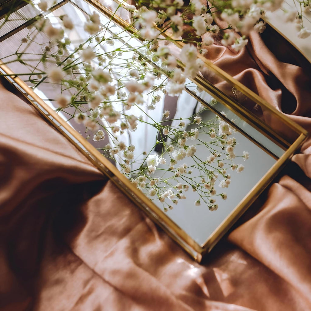 Gold-tone mirrored vanity tray styled with white flowers; decorative flowers not included.